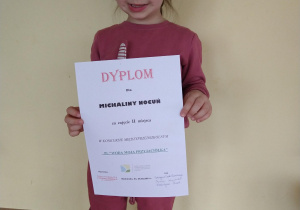 Dziewczynka trzyma dyplom za zajęcie II miejsca w konkursie plastycznym.